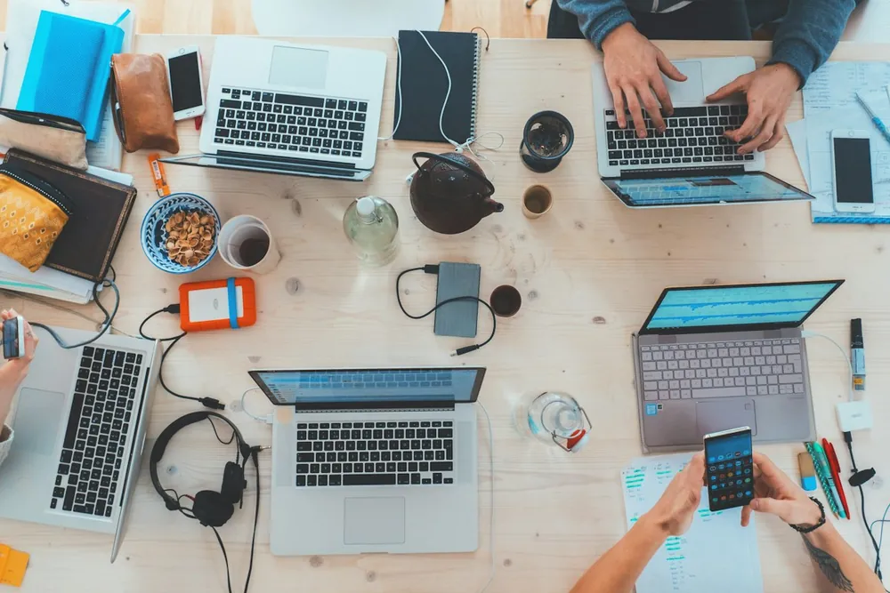 Mesa de trabajo compartida con portátiles y personas trabajando en equipo